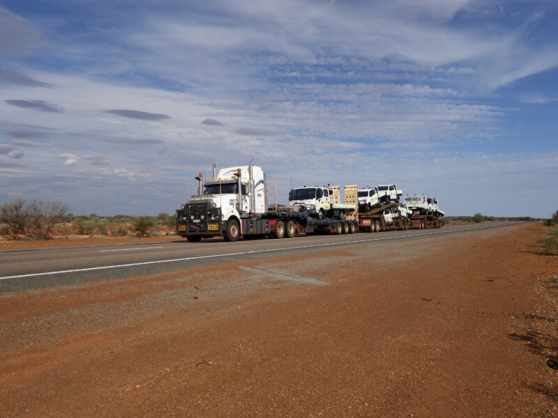 Road train carrying freight along a red dirt road through the Australian outback