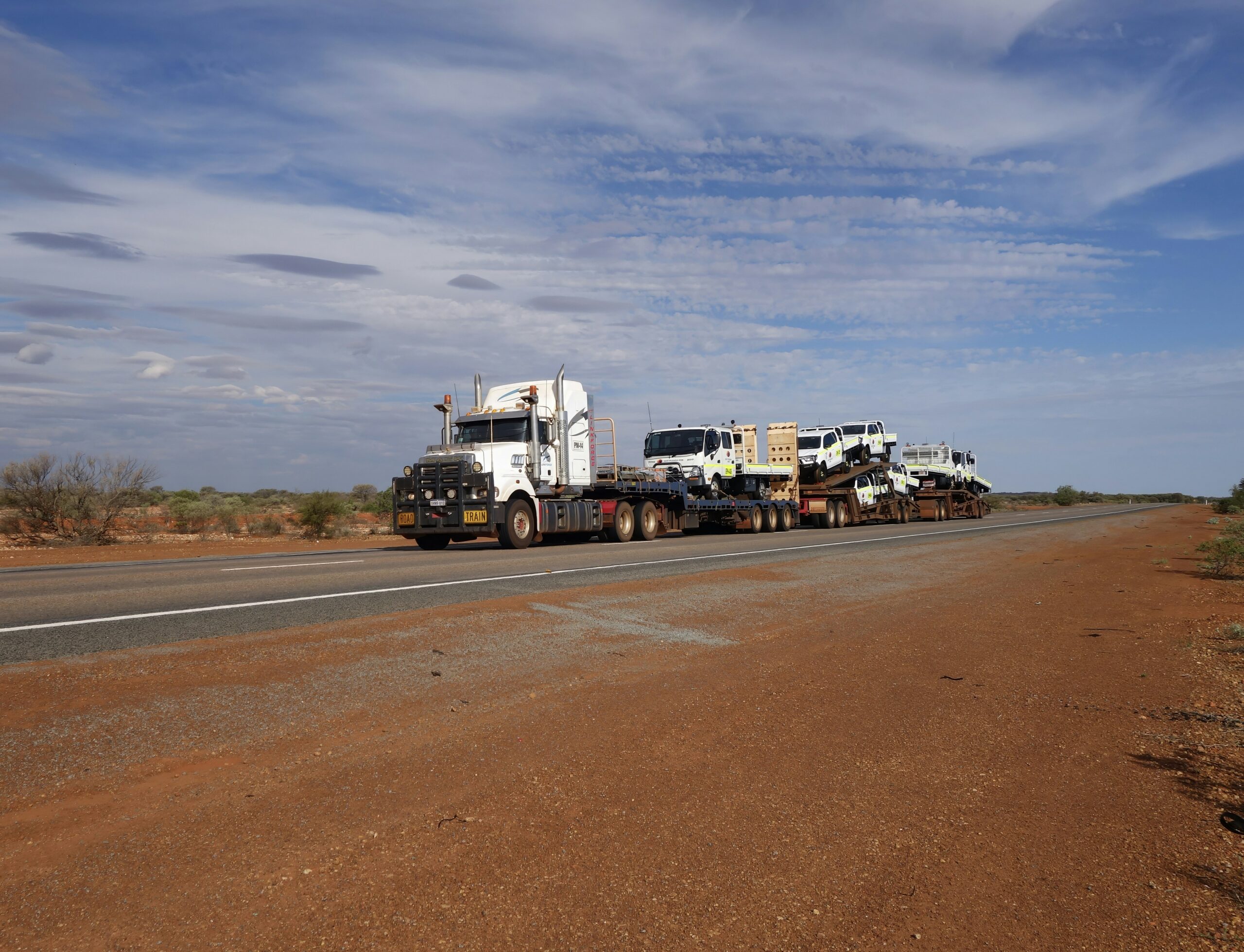 Road train carrying freight along a red dirt road through the Australian outback